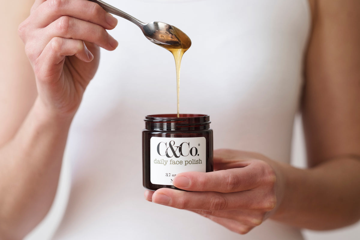 Spoonful of honey-based cleanser dripping into jar